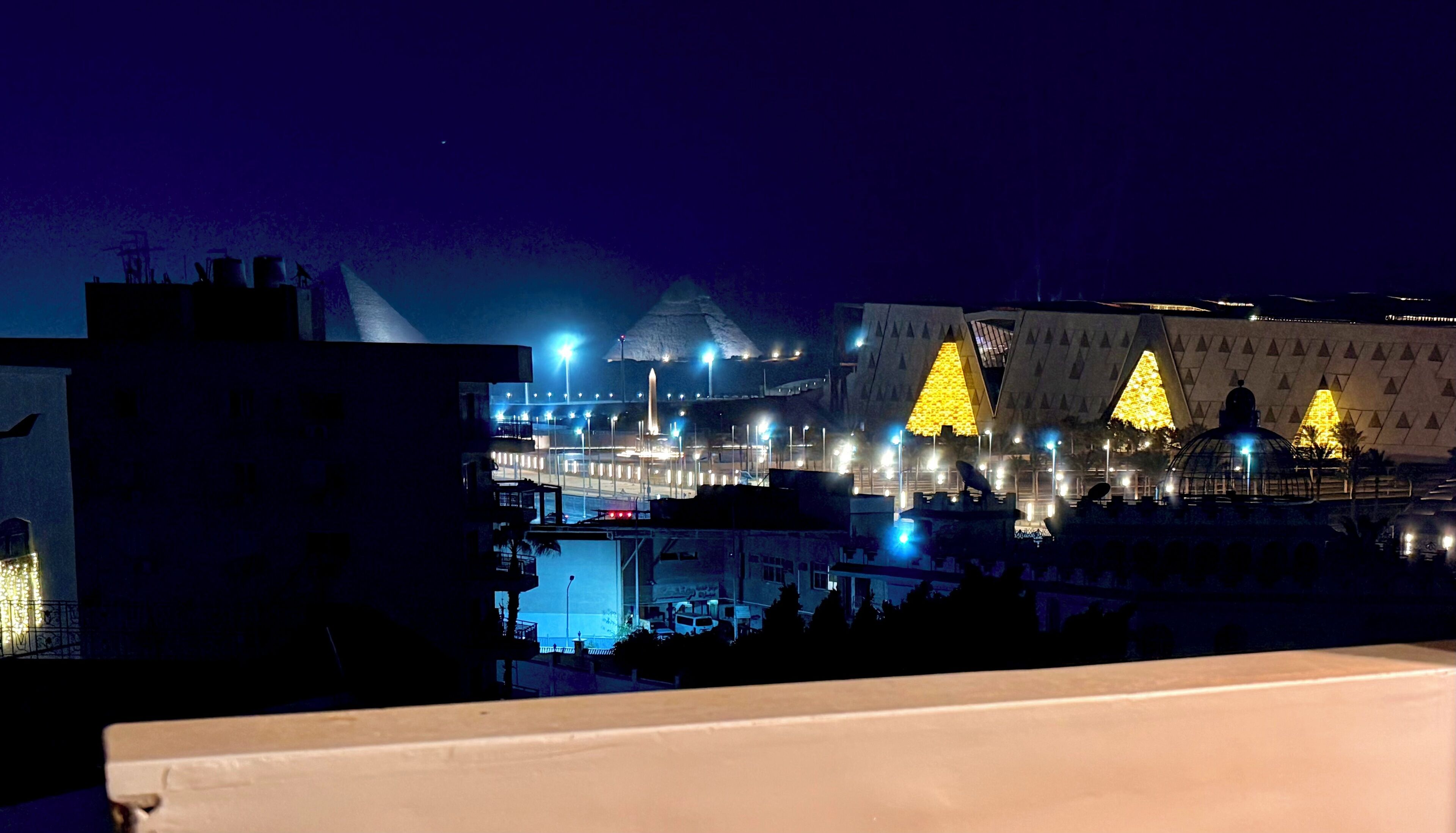 A nighttime view of a building with illuminated triangular structures and a dome.