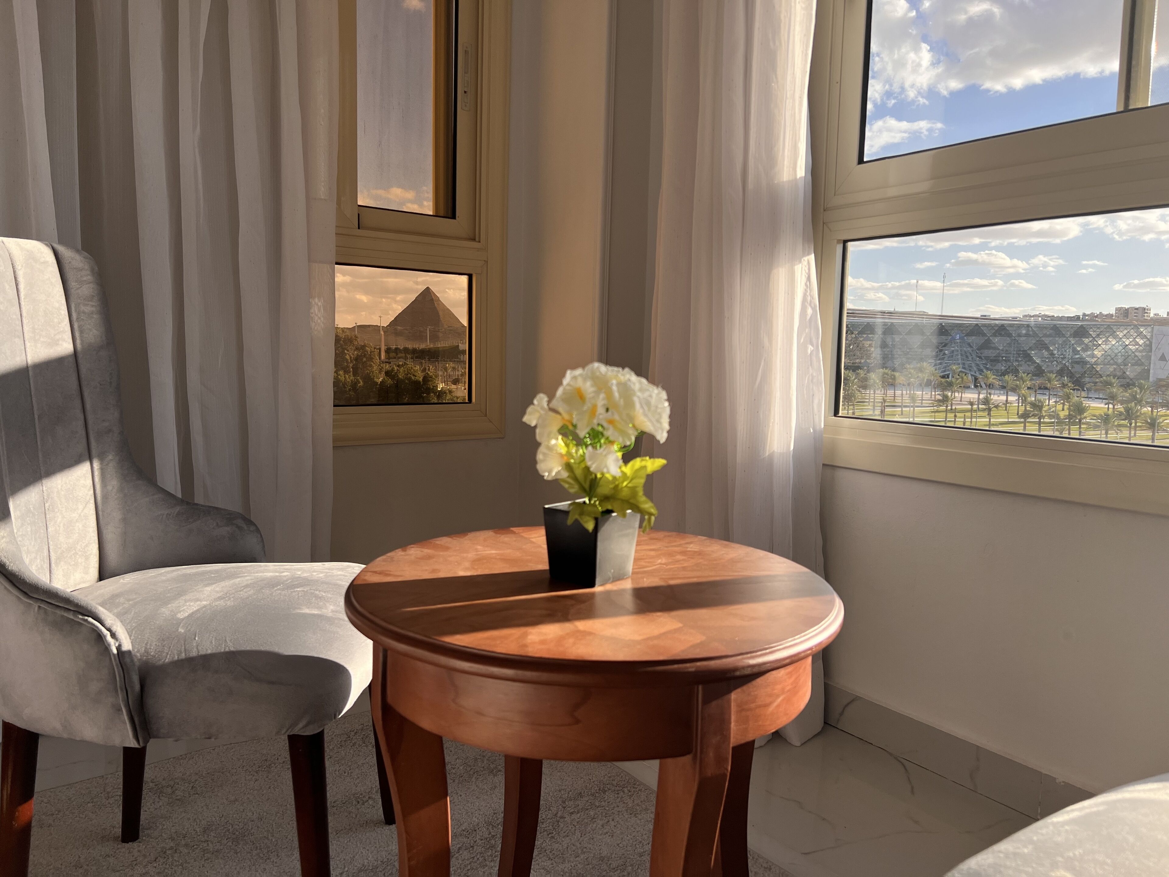 A room with a view of a cityscape, a table with a vase of flowers, and a chair.