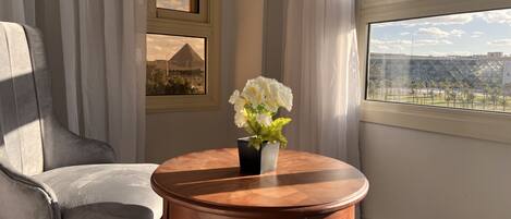 A room with a view of a cityscape, a table with a vase of flowers, and a chair.