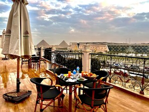 A balcony with a view of the pyramids, a table with chairs, and umbrellas.