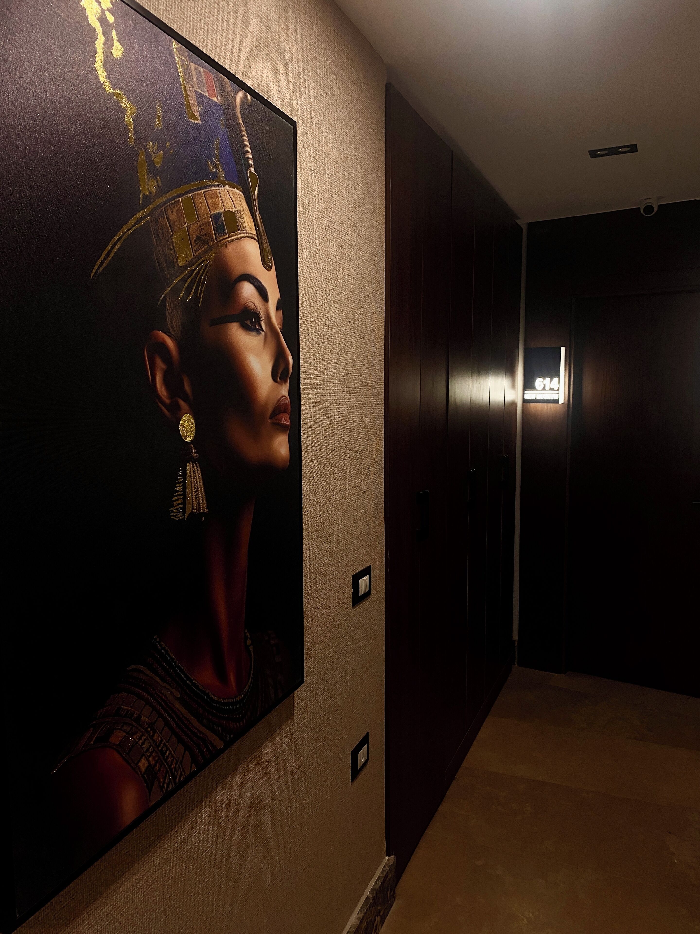 A hallway with a large wall mural, a door with a number sign, and a light fixture on the ceiling.