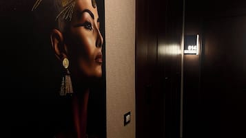 A hallway with a large wall mural, a door with a number sign, and a light fixture on the ceiling.