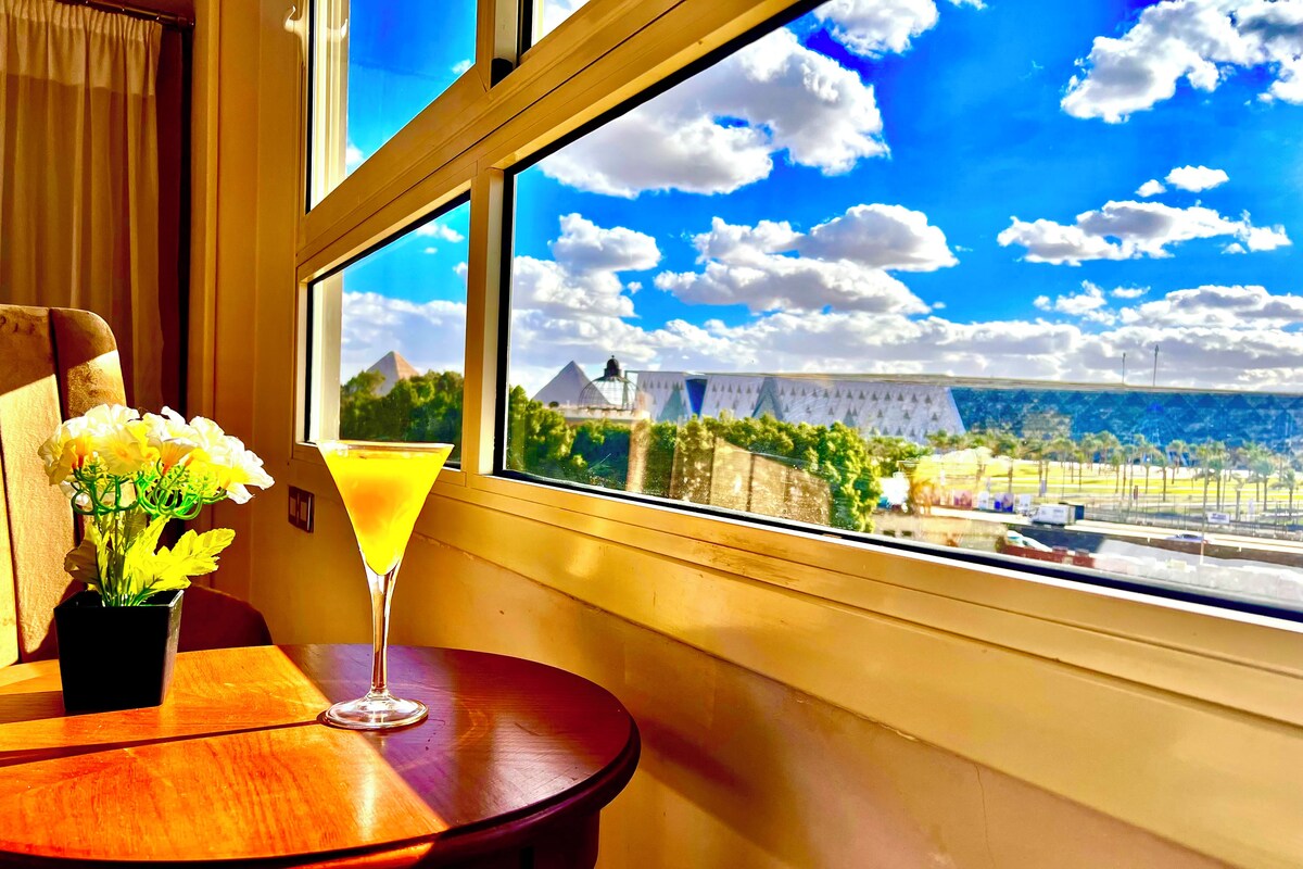 Una habitación con un ventanal grande, una mesa con un florero y una copa de martini.