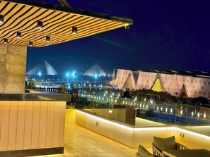 A rooftop terrace with a view of pyramids and a modern building at night.