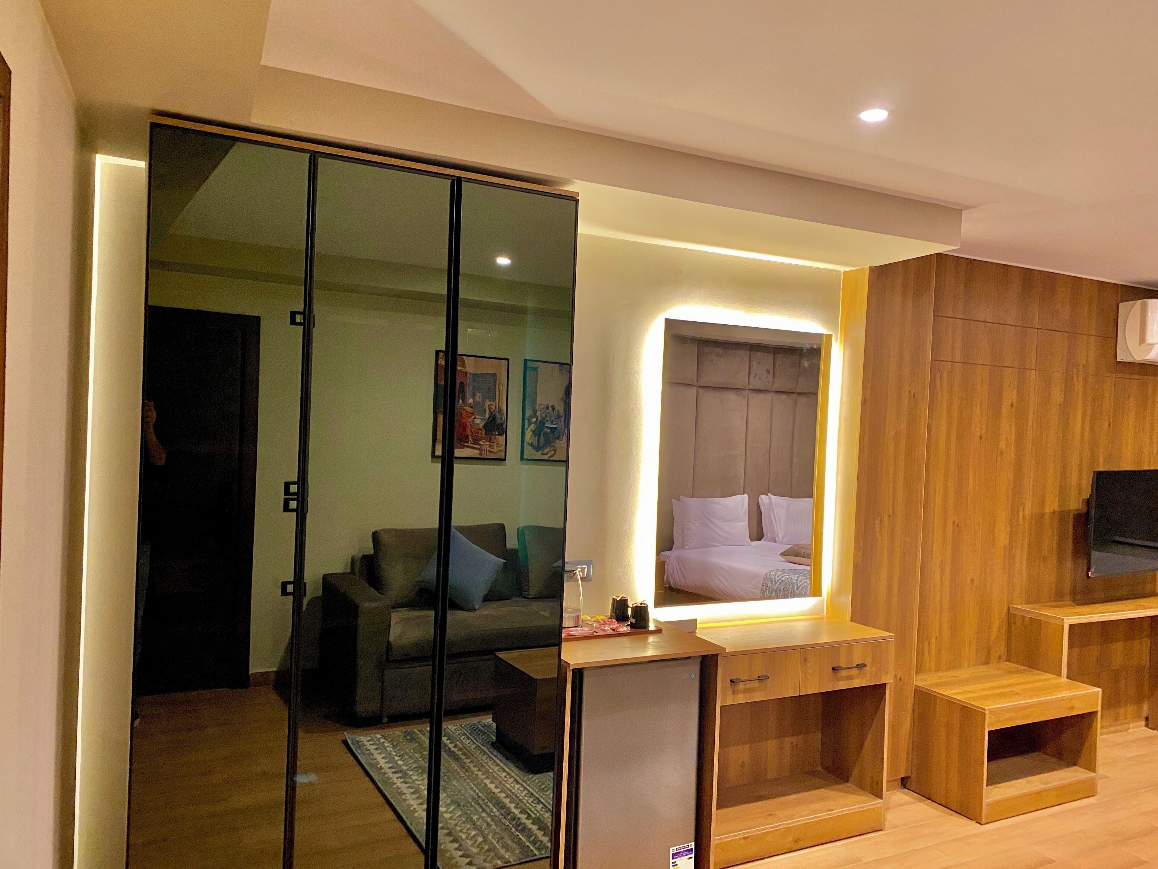 A modern bedroom with a large mirror, a bed, a wooden wardrobe, and a small desk area.