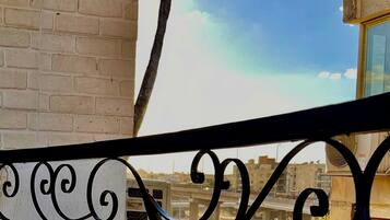 A balcony with a metal railing, a brick wall, and a view of a cityscape including buildings and a bridge.