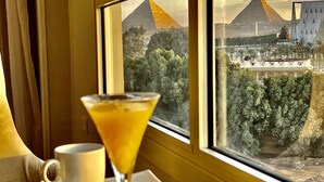Una mesa con una copa de martini y una taza, con vista a pirámides y un edificio moderno.
