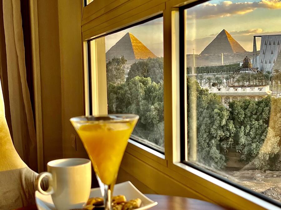Una mesa con una copa de martini y una taza, con vista a pirámides y un edificio moderno.