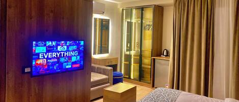 Ein modernes Hotelzimmer mit Fernseher, der eine Auswahl an Filmen zeigt, einer Couch, einem Couchtisch, einem Kleiderschrank und einem Bett.