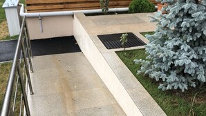 Un chemin en béton mène à un banc en bois muni d’une rambarde métallique d’un côté.
