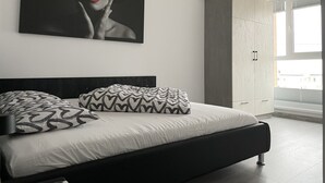 Une chambre à coucher moderne avec un grand lit, un coussin aux motifs noir et blanc, une grande peinture abstraite et une armoire.