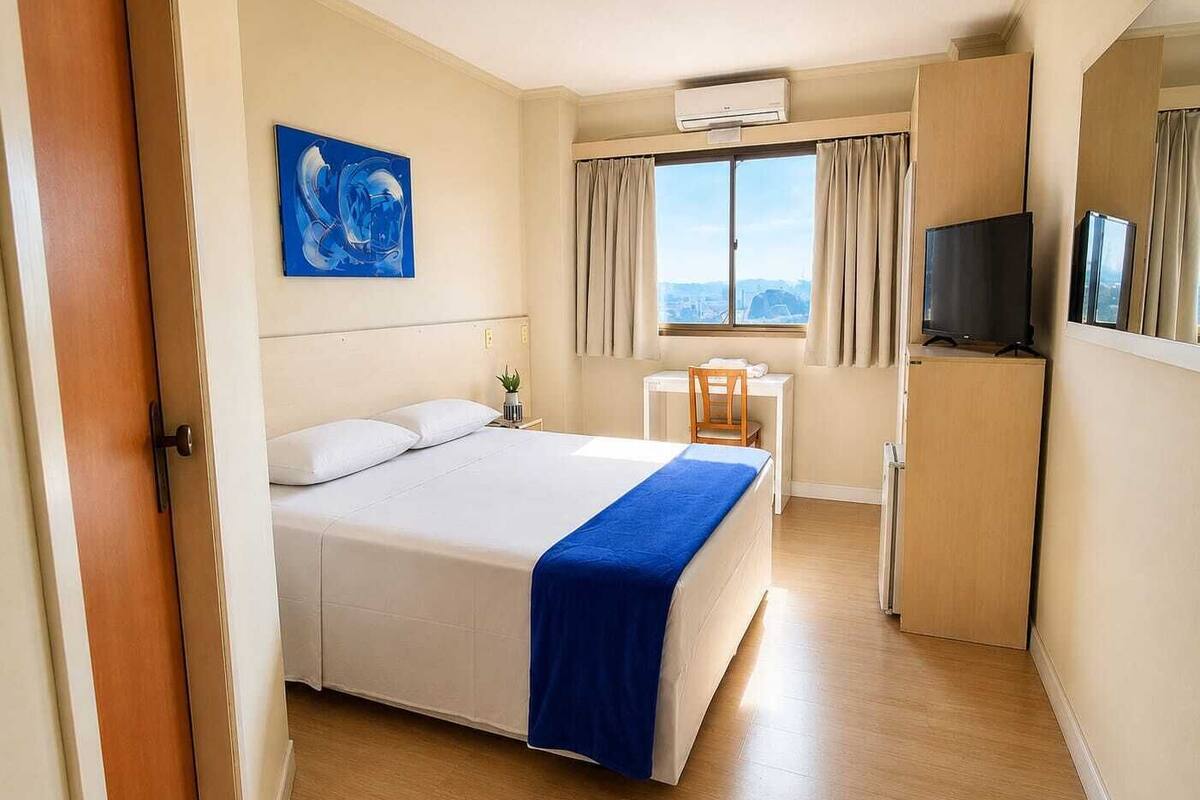 Une chambre d’hôtel équipée d’un lit, d’un bureau, d’une chaise, d’une télévision et d’une fenêtre avec des rideaux.
