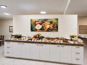 A buffet counter with various food items, a painting of fruits on the wall, and a white cabinet with drawers. - KLEIN VILLE  ESTEIO EXPRESS BR (Esteio)