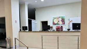 Zona de recepción de un hotel con mostrador, computadoras, un florero y una escalera.