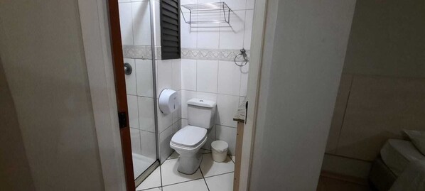 Un baño pequeño con azulejos, un inodoro, un secador de manos y un dispensador de papel higiénico.