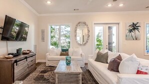 A living room with a TV, white sofas, a coffee table, and a large mirror.