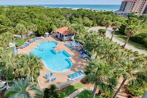 A pool with a unique shape surrounded by lounge chairs and umbrellas, set in a lush green area with palm trees. - LABOR DAY WEEKEND MAKE AN OFFER! Tops'l Resort 2BR Beach, Pool, Awesome View! (Miramar Beach)