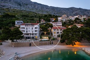Un hotel sul lungomare con diversi piani, una piscina e uno sfondo montuoso.