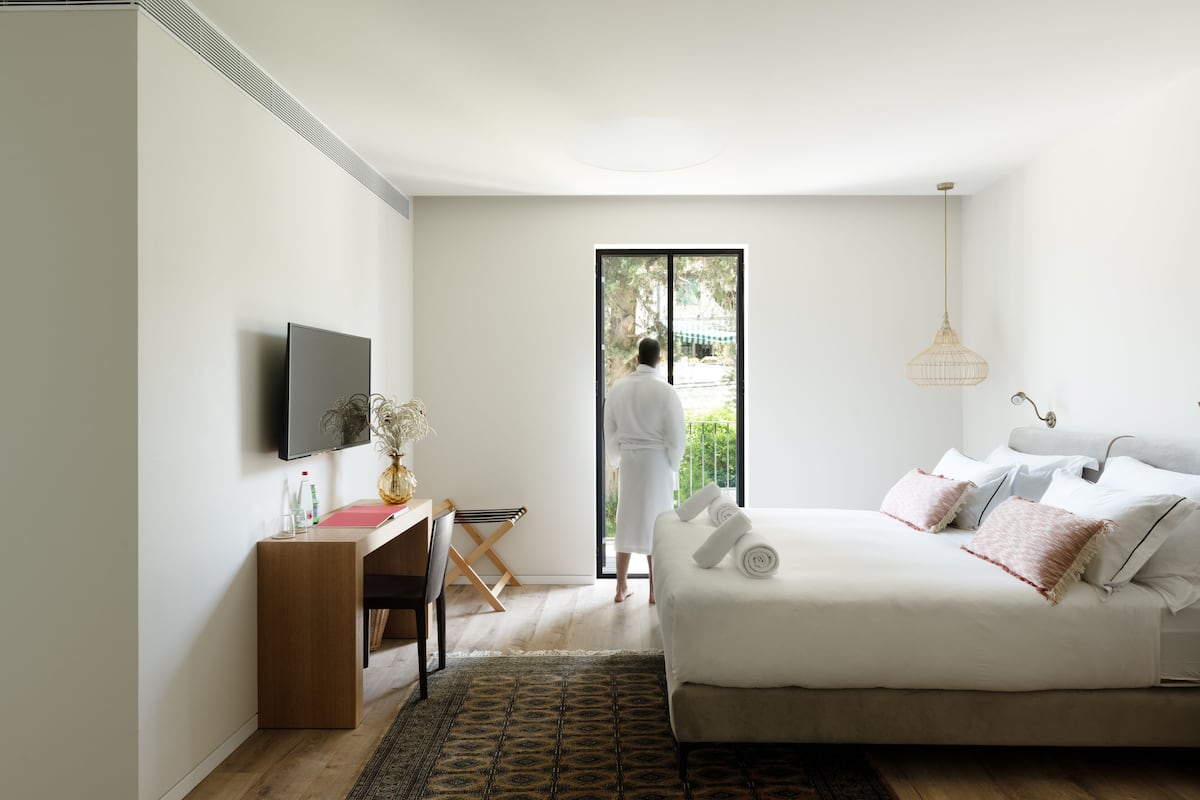 A bedroom with a bed, a desk, a chair, a TV, and a window.