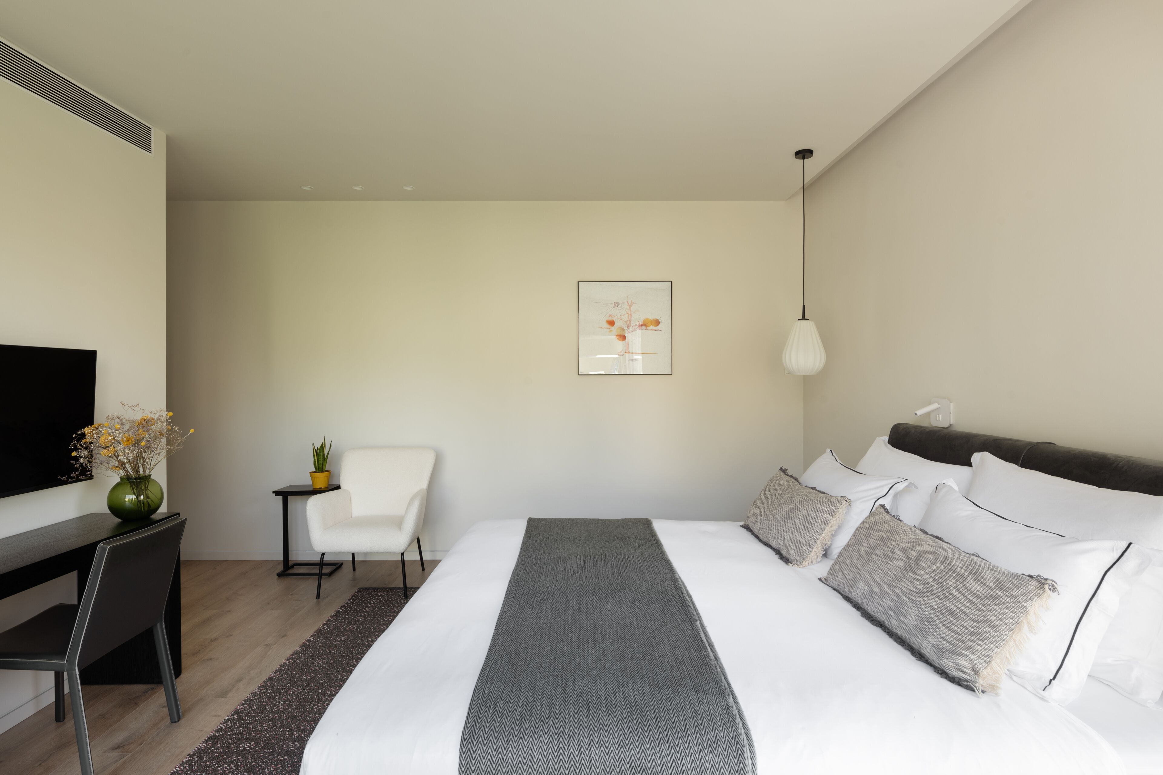 A modern hotel room with a large bed, a desk, a chair, and a TV.