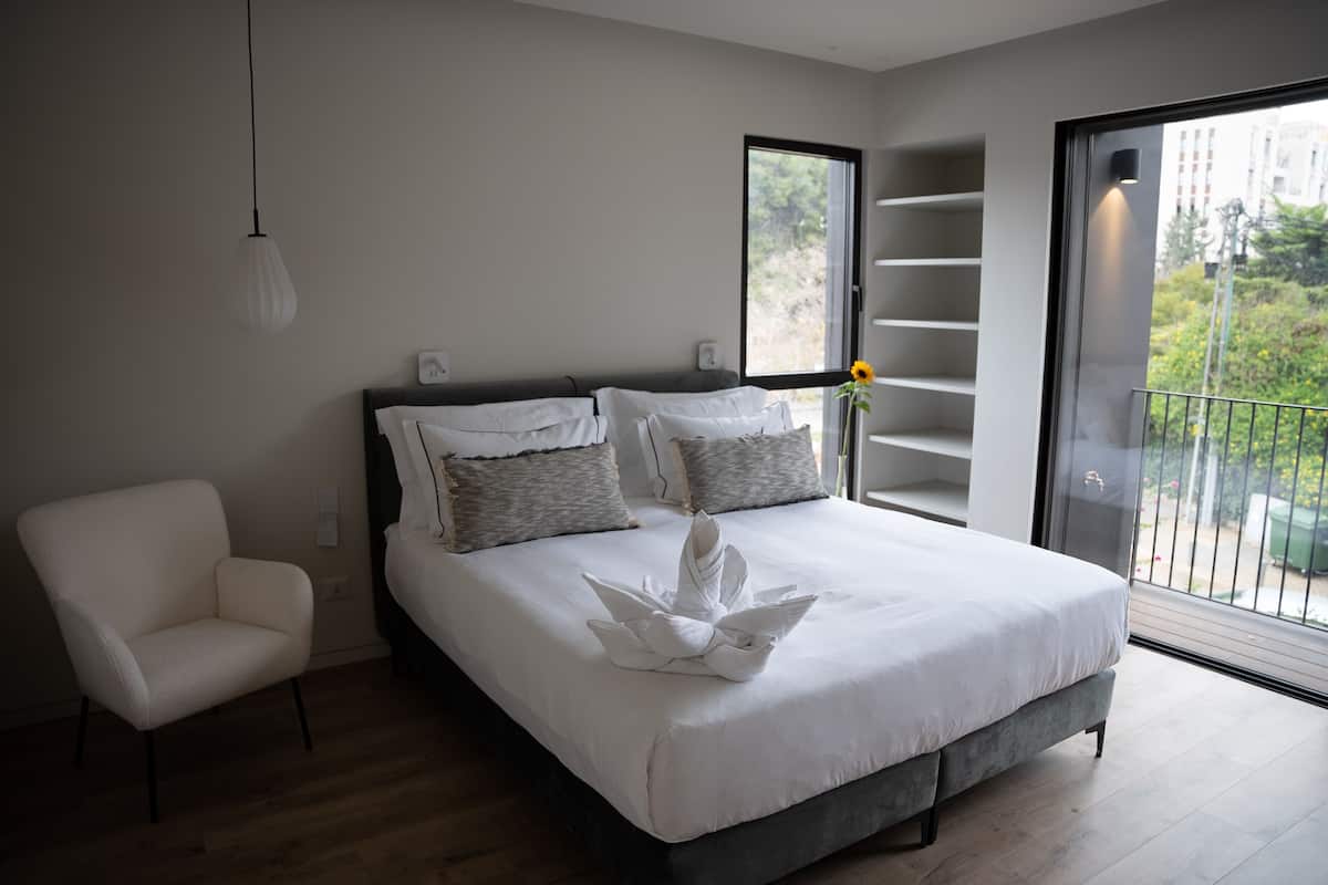 A modern bedroom with a bed, a chair, a window, and a balcony.