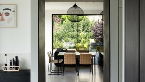 Una cocina moderna con un área de comedor visible a través de un acceso abierto. Dos lámparas colgantes iluminan la mesa del comedor.