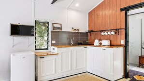 Cocina compacta con armarios blancos, encimera de madera, microondas integrado y ventana con vistas a la vegetación.