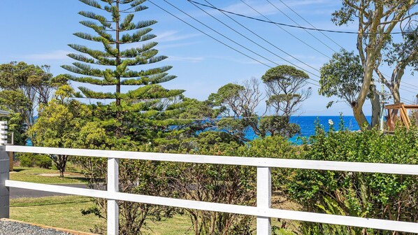 A coastal property with a white fence, lush greenery, and a view of the sea.