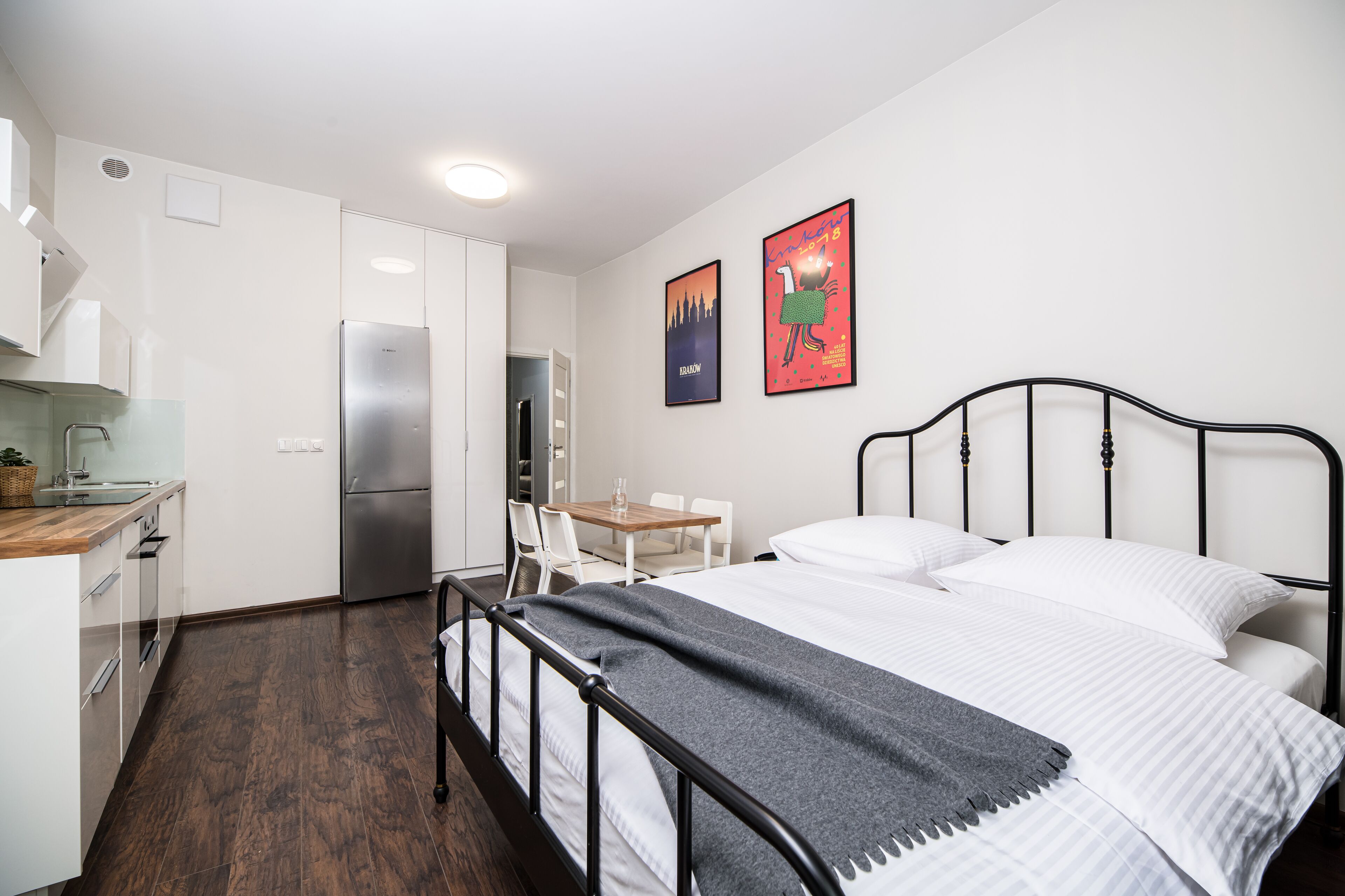 A modern hotel room with a bed, a desk, and a kitchenette.