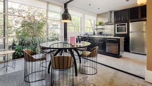 Een moderne keuken met een centraal eiland, grote ramen en een eethoek met stoelen.
