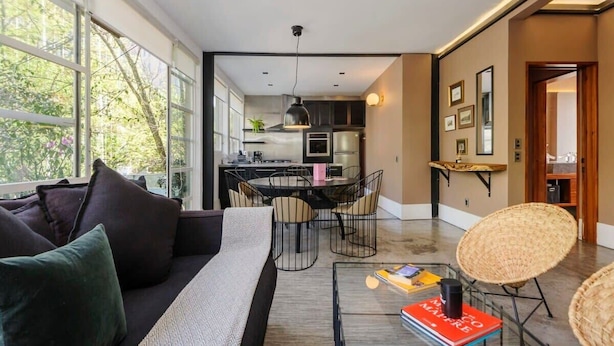 Een moderne woonkamer met een bank, salontafel en rieten stoelen. Op de achtergrond is een eethoek met een tafel en stoelen zichtbaar.