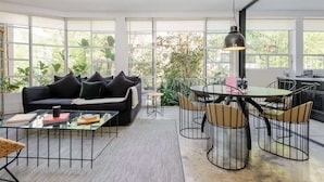 Een moderne woonkamer met een zwarte bank, een glazen salontafel, en een eethoek met een ronde tafel en stoelen.
