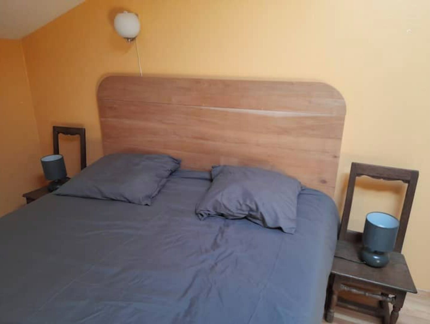 Une chambre à coucher avec une tête de lit en bois, deux oreillers, une table de chevet avec une lampe et un miroir.