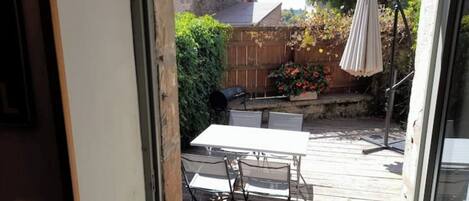 A wooden deck with a table and chairs, a barbecue grill, and a patio umbrella.