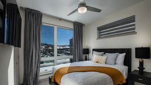 A modern bedroom with a large bed, a ceiling fan, a nightstand, and a window with curtains.