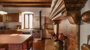 A rustic kitchen with wooden beams, a brick fireplace, and a dining area with a table set for two.