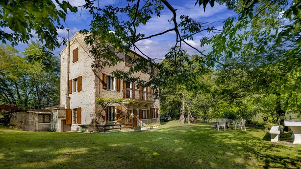 A rustic stone building with a balcony, surrounded by a well-maintained lawn and trees.