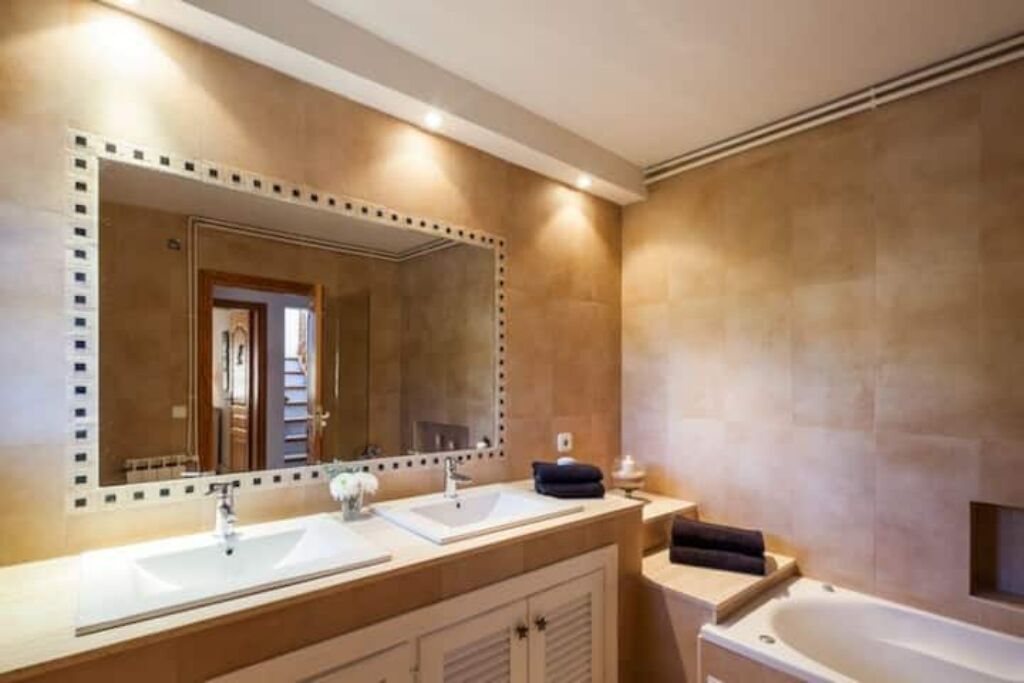 Une salle de bain dotée d’un grand miroir, de deux lavabos, d’une baignoire et d’un meuble-lavabo avec un porte-serviettes.