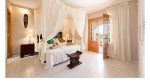 A bedroom with a four-poster bed, a nightstand, a bedside table, and a view of the outside.