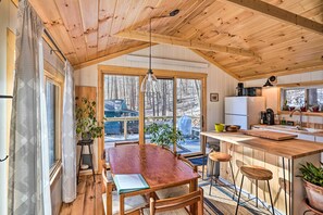 En mysig stuga med en inredning som inkluderar ett matbord i trä, en bardisk och stora fönster med utsikt över det snötäckta landskapet.