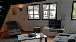 Ein modernes Wohnzimmer mit einem grauen Ecksofa, einem kleinen Couchtisch, einem Fernseher auf einem weißen Schrank und einer Treppe, die zu einer oberen Ebene führt.