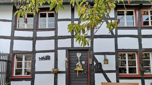 Ein traditionelles Fachwerkhäuschen mit Holztür, Fenstern und einer kleinen Außenbestuhlung mit Tisch und Stühlen.