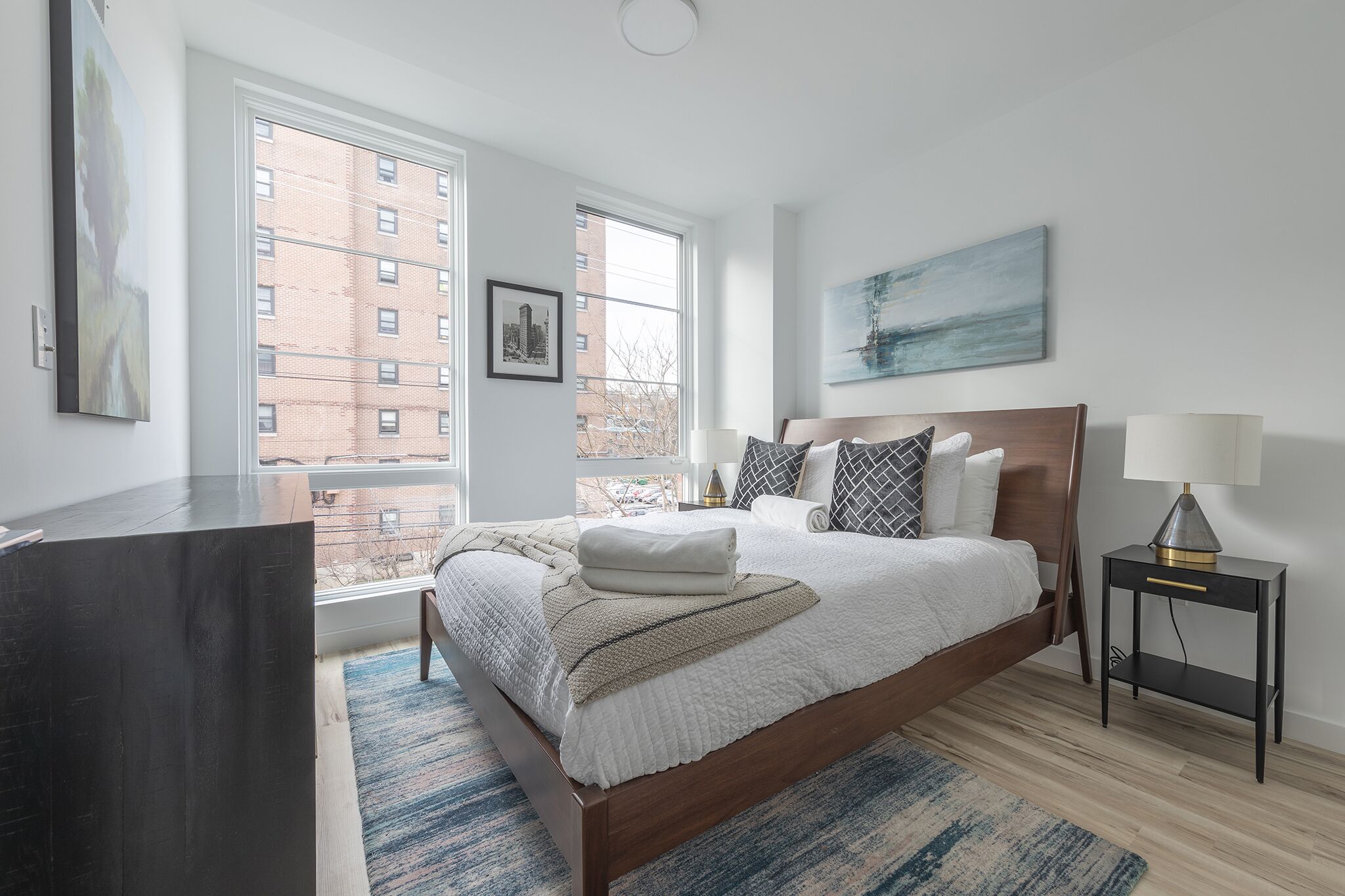 A modern bedroom with a large bed, a bedside table, a lamp, and a window with a city view.