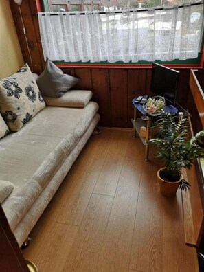 Een kleine kamer met een bank, een tafeltje met een plant en een raam met gordijn.