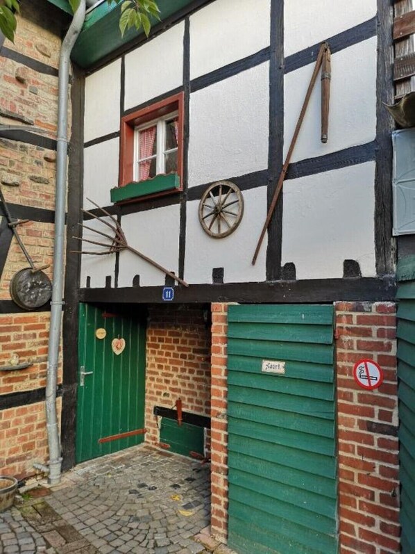 Un edificio tradicional de entramado de madera con una puerta verde, una ventana con cortina roja y un cartel de prohibido fumar.