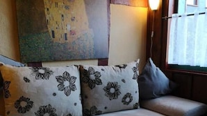 A sofa with floral cushions, a painting above it, and a window with curtains. - Monty's vacation home (Simmerath)