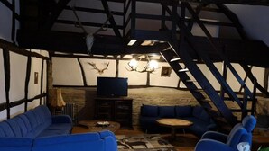 Une pièce rustique avec des poutres apparentes, un mur en pierre, un canapé bleu, une table basse en bois et un téléviseur posé sur un meuble.