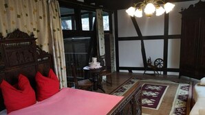 Une chambre à l’ancienne, dotée d’un grand lit, d’une tête de lit en bois, d’un lustre et offrant une vue sur l’extérieur grâce à une fenêtre agrémentée de rideaux.