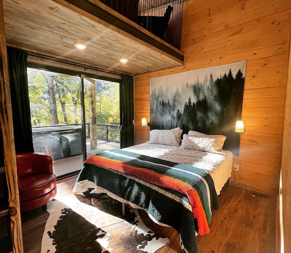 Ein Schlafzimmer mit einem großen Bett, Blick ins Freie und einer Holzbalkendecke.