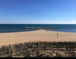 Een zandstrand met een houten omheining op de voorgrond en een rotsenrijke zeebaan op de achtergrond.